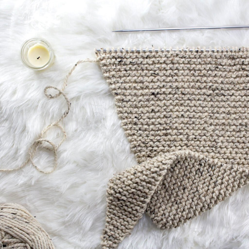 asymmetrical triangle shawl in the process of being knitted on knitting needles on a faux fur blanket