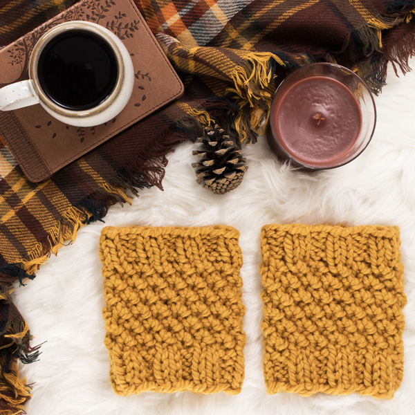 cozy scene of a knit boot cuffs on a faux fur blanket with coffee, candle & a journal.