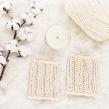 cozy scene of a knit boot cuffs on a faux fur blanket with a candle & cotton bolls.