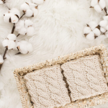 cozy scene of a knit boot cuffs in a basket on a faux fur blanket with cotton bolls.