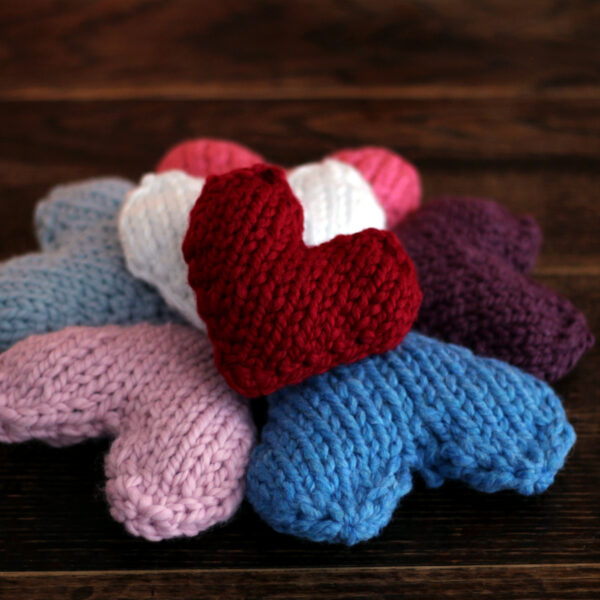 pile of knitted hearts in various colors displayed on a dark wood table.