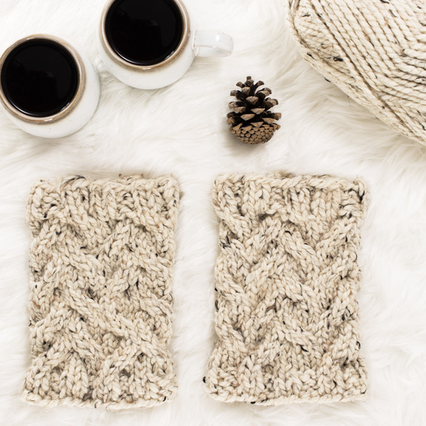 cozy scene of a cable knit boot cuffs on a faux fur blanket with coffee & a pine cone.