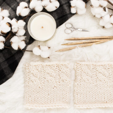 cozy scene of a cable knit boot cuffs on a faux fur blanket with a candle & knitting needles.