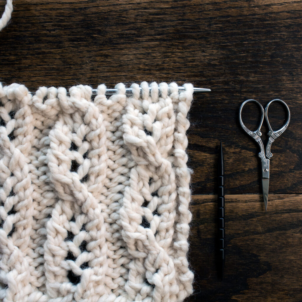 Swatch of the Cable Lace Knitting Stitch Pattern on a wood table.