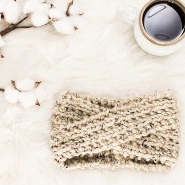 chunky knit twist headband on a fur blanket with knitting needles & a coffee