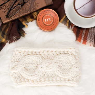 cozy scene of a chunky cable knit headband on a fur blanket with hot tea & knitting needles.