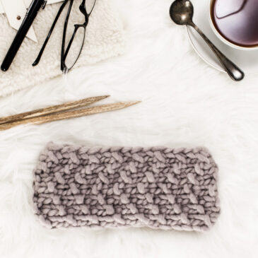 cozy scene of a chunky chevron knit headband on a fur blanket with hot tea & knitting needles.