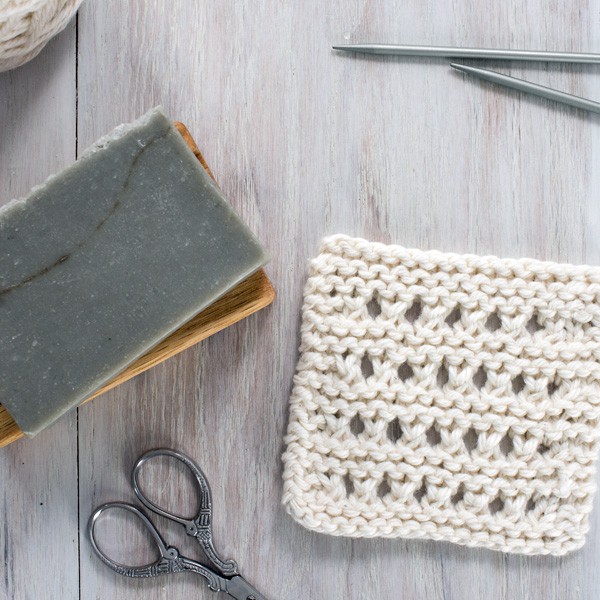 small knitted dishcloth with soap, scissors and knitting needles