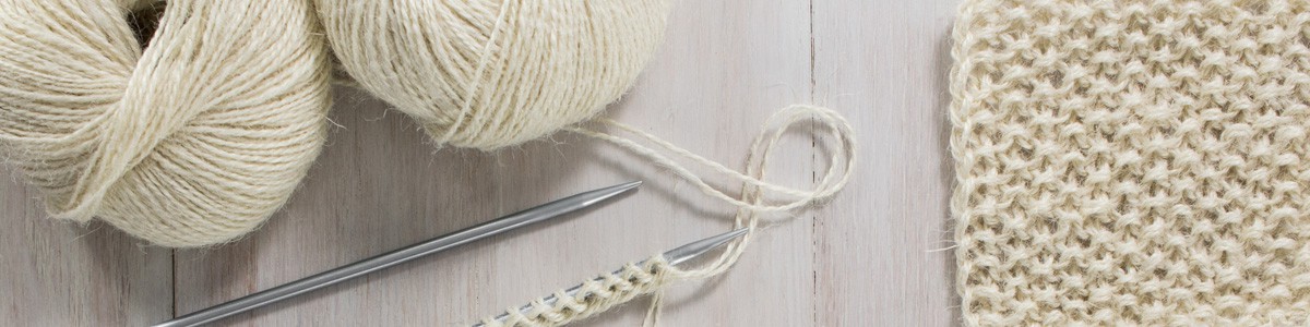 2 balls of yarn with 2 swatches and 2 knitting needles
