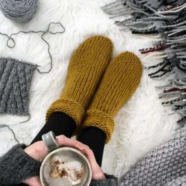 a cozy setting with chunky knitted socks, coffee, leaves on a fur blanket.