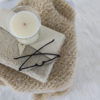 knit scarf on a fur blanket with a candle, journal and eyeglasses