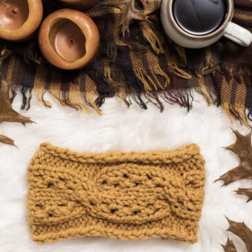 cozy scene of a cross cable knit headband on a fur blanket with coffee & a candle on a flannel blanket