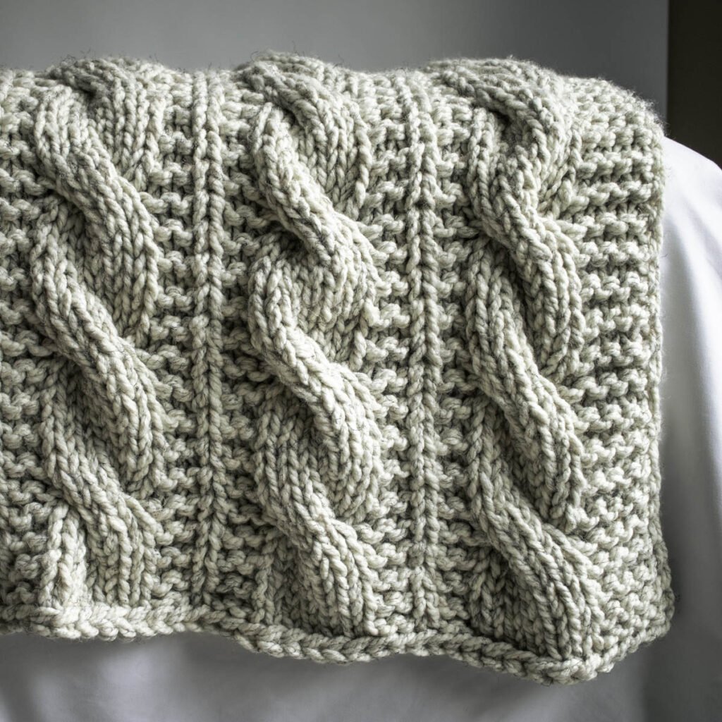 Close-up of the A Beautiful Journey Blanket in super bulky yarn, showing the chunky texture and cozy drape of the cable knit stitch.