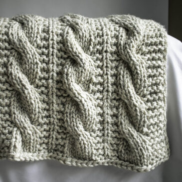 Close-up of the A Beautiful Journey Blanket in super bulky yarn, showing the chunky texture and cozy drape of the cable knit stitch.