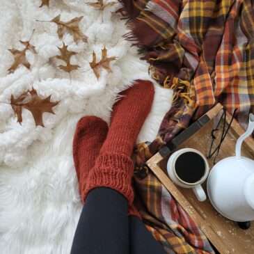 a cozy setting with worsted knitted socks, coffee, leaves on a fur blanket.
