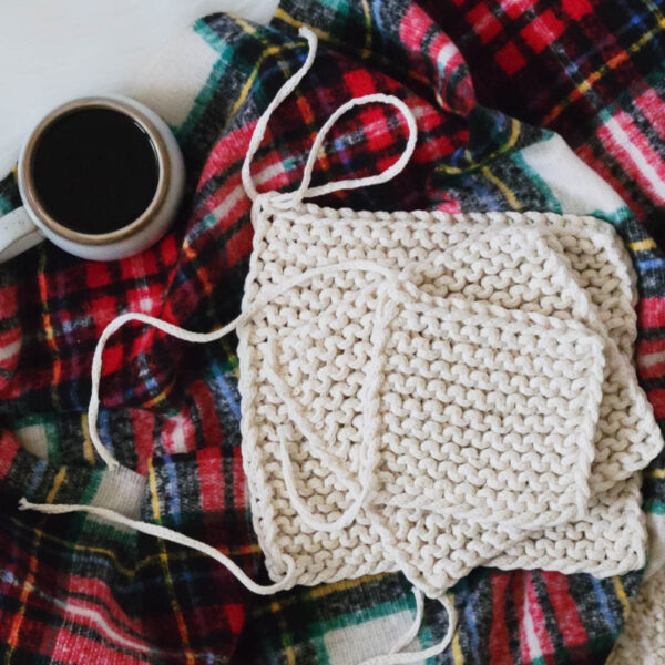 3 garter stitch knit potholders on a plaid blanket displayed with a cup of coffee and tails not woven in