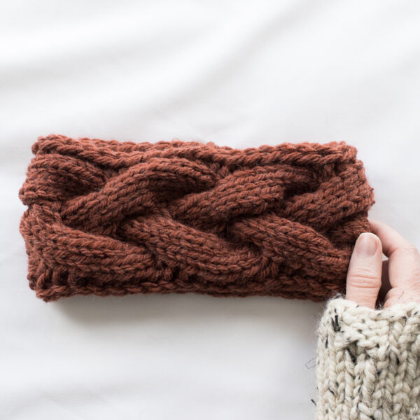 Chunky Braided Cable Headband held by one hand laying on a white background.
