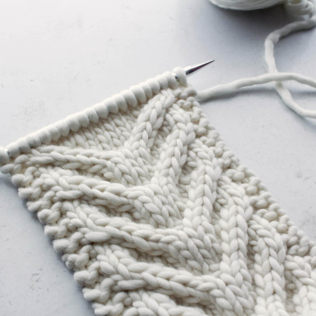 chunky cable knit headband, still on the needles, on a white table