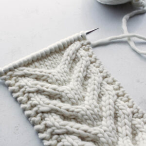 chunky cable knit headband, still on the needles, on a white table