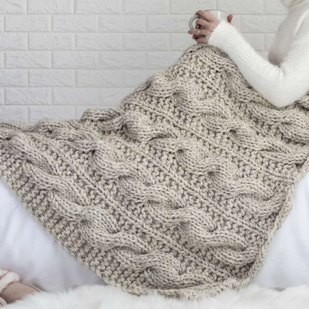 cable knit blanket laying across someone's lap draped over the bed.