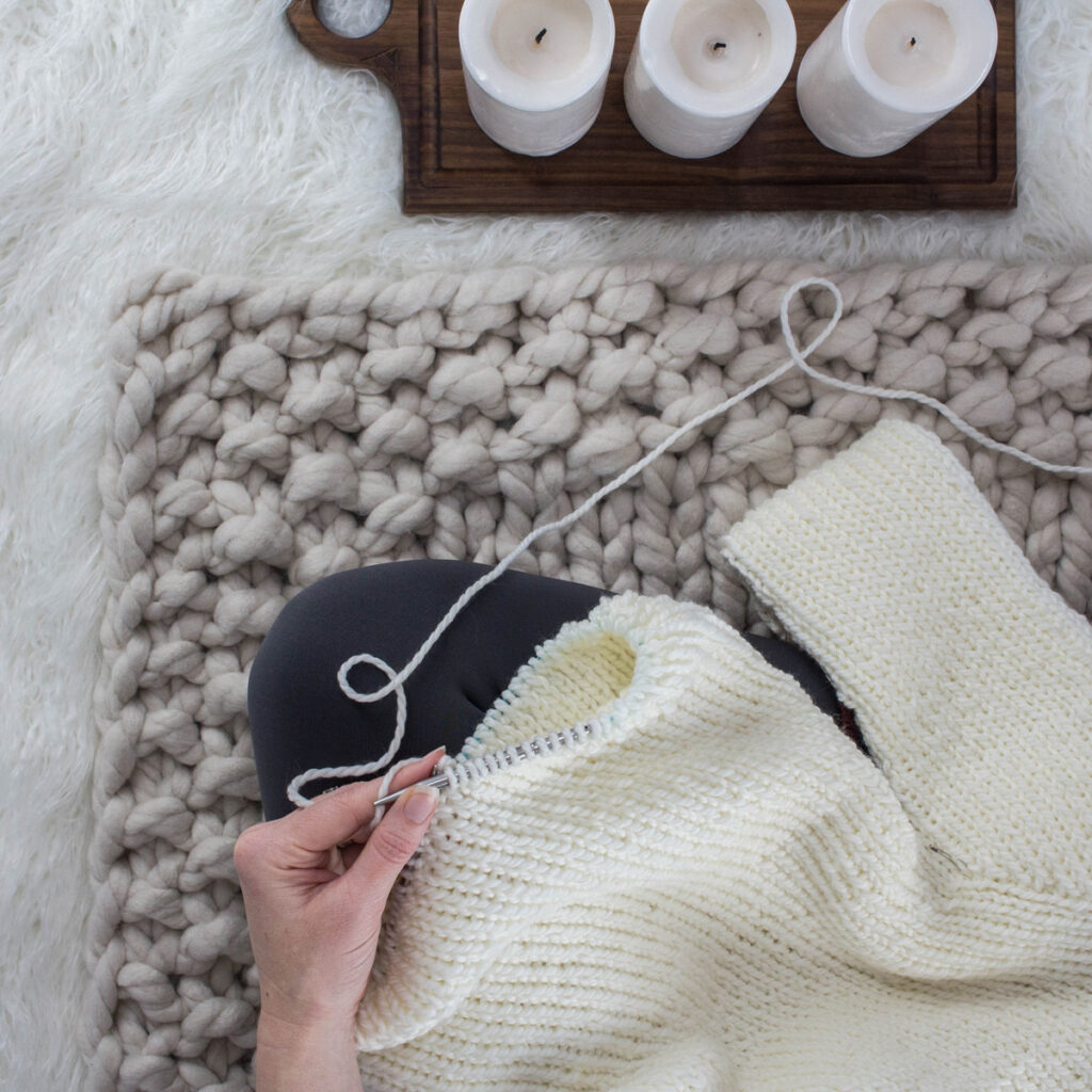 model sitting on a jumbo knit blanket while knitting