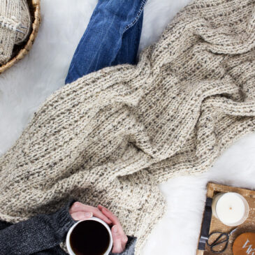 Model snuggled up in a cable knit blanket with a cup of coffee.