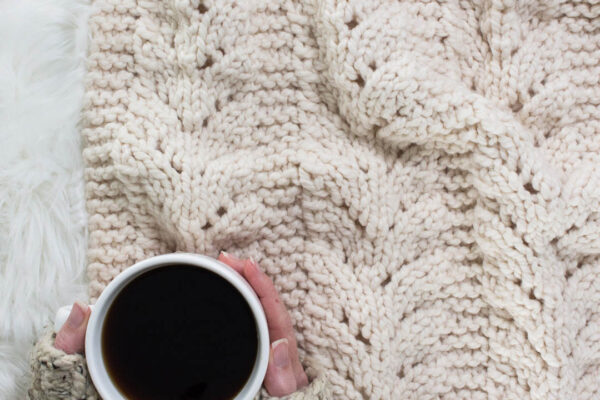partially knit lace blanket on a faux fur blanket with a cup of coffee.
