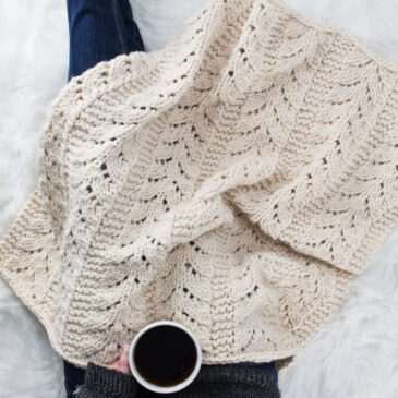 Model snuggled up in a chunky lace knit blanket with a cup of coffee.