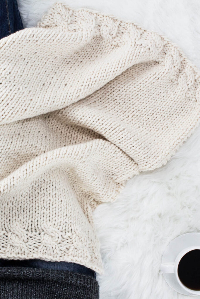 Model snuggled up in a chunky lace knit blanket with a cup of coffee.