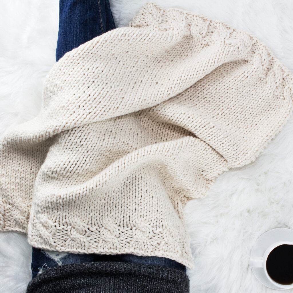 Model snuggled up in a chunky lace knit blanket with a cup of coffee.