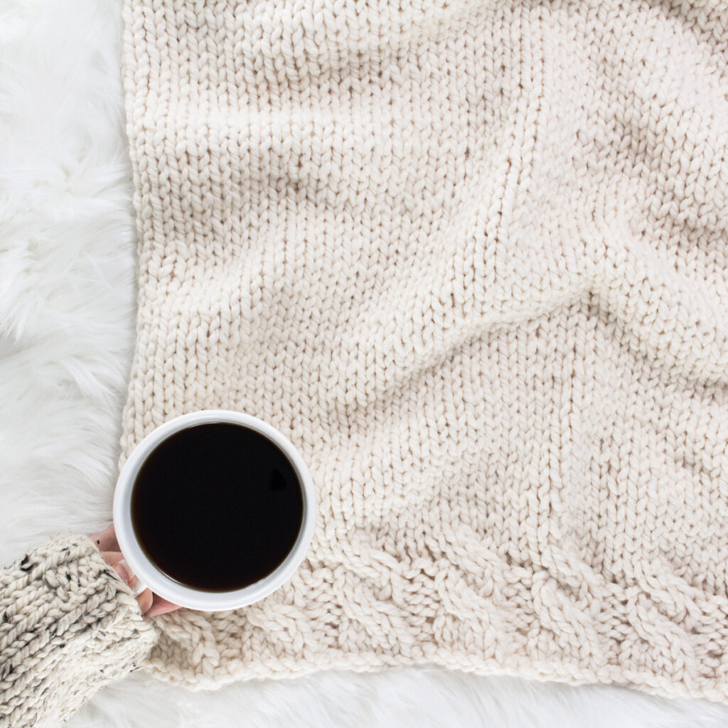Chunky cable knit blanket on a faux fur blanket with a cup of coffee.