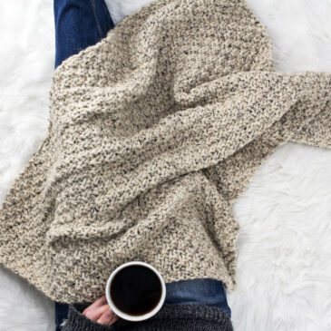 Model snuggled up in a beginner hand knit blanket with a cup of coffee.