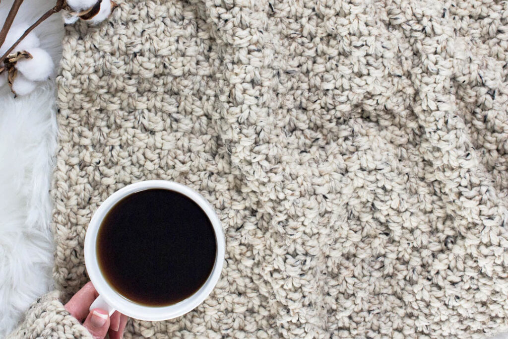 beginner hand knit blanket on a faux fur blanket with a cup of coffee.