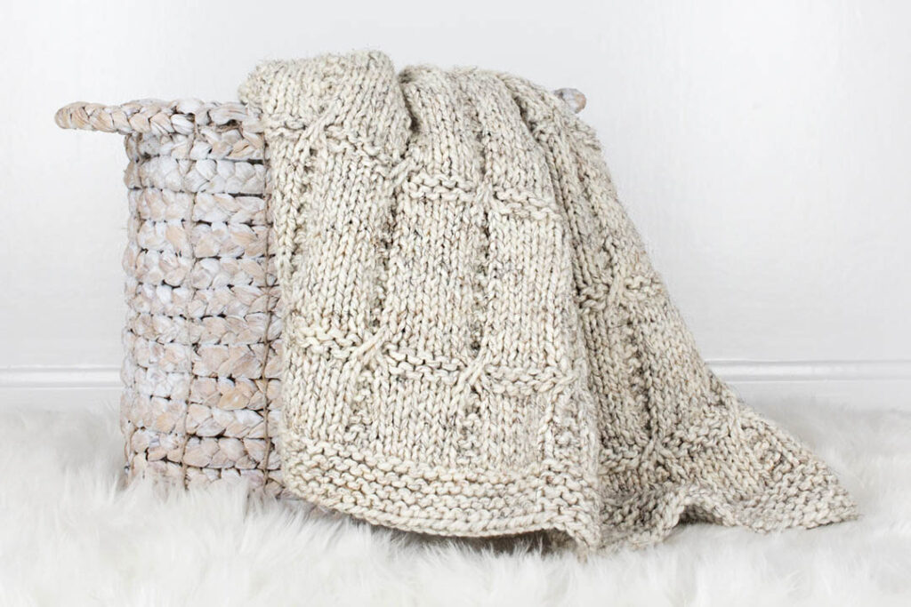 hand knit chunky blanket draped over a basket