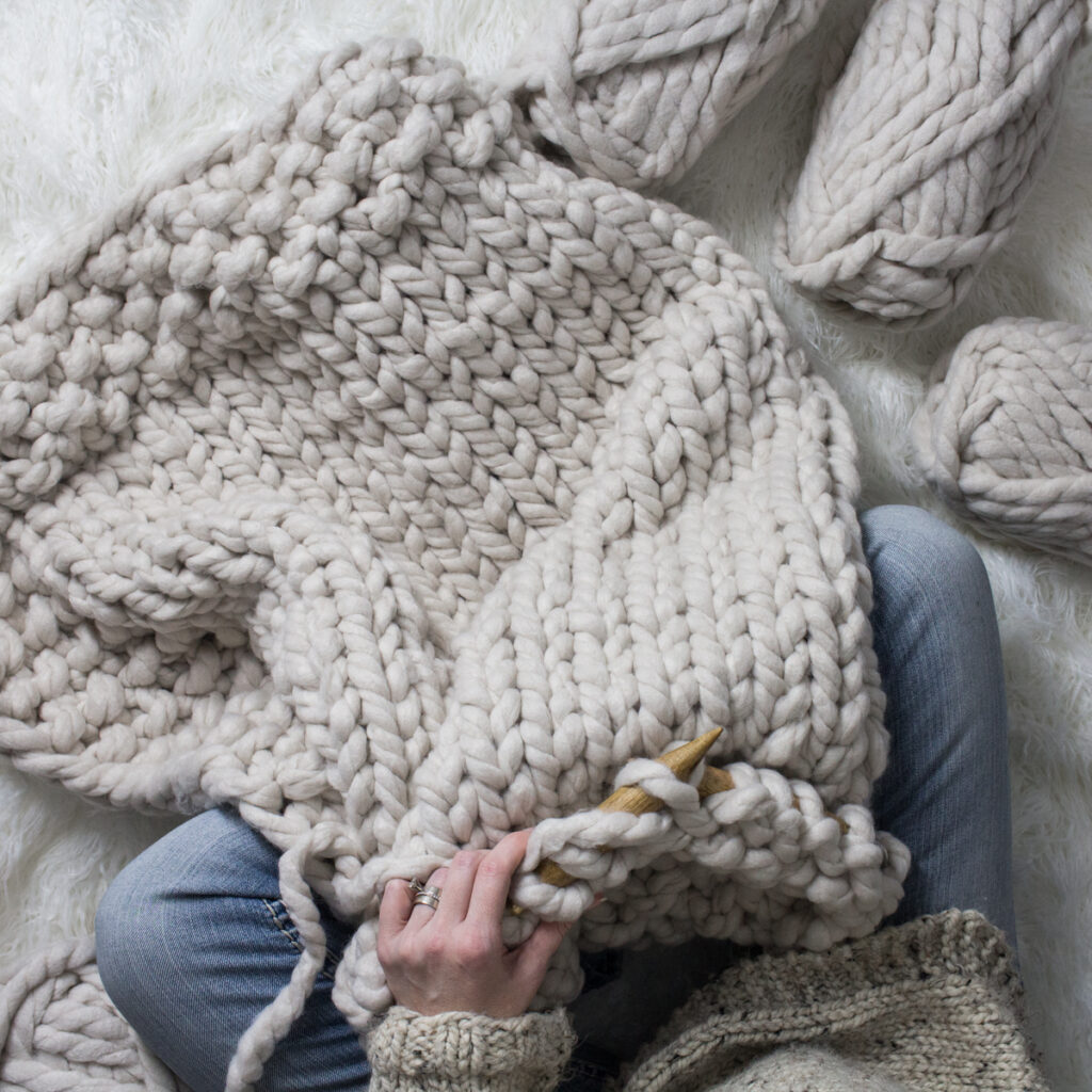 someone knitting a jumbo blanket with jumbo knitting needles