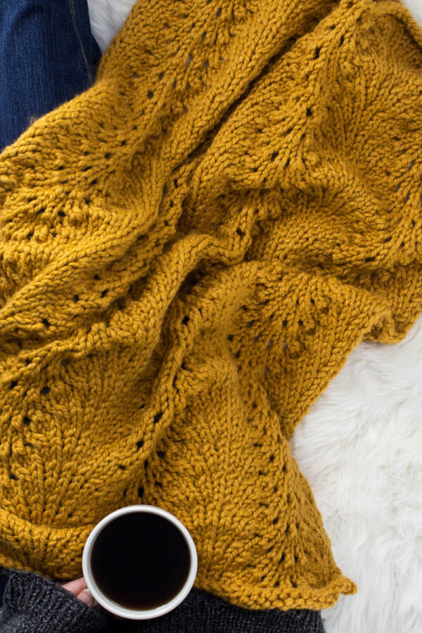 Model snuggled up in a cable knit blanket with a cup of coffee.