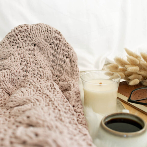 Model snuggled up in a cable knit blanket with a cup of coffee.