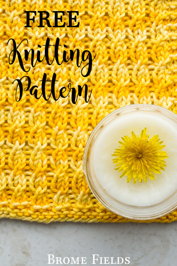 pic of a cable knitted dishcloth on a table with a jar of handmade dandelion lotion with a dandelion head in it.