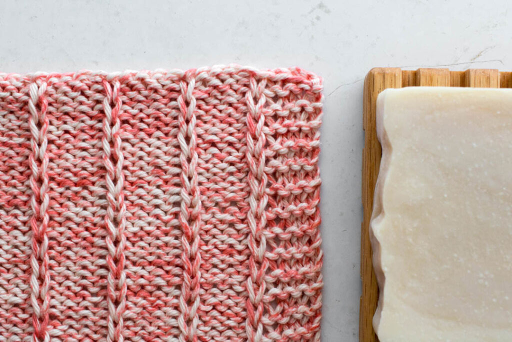 pic of a knit dishcloth on a table with a bar of soap on a wooden tray