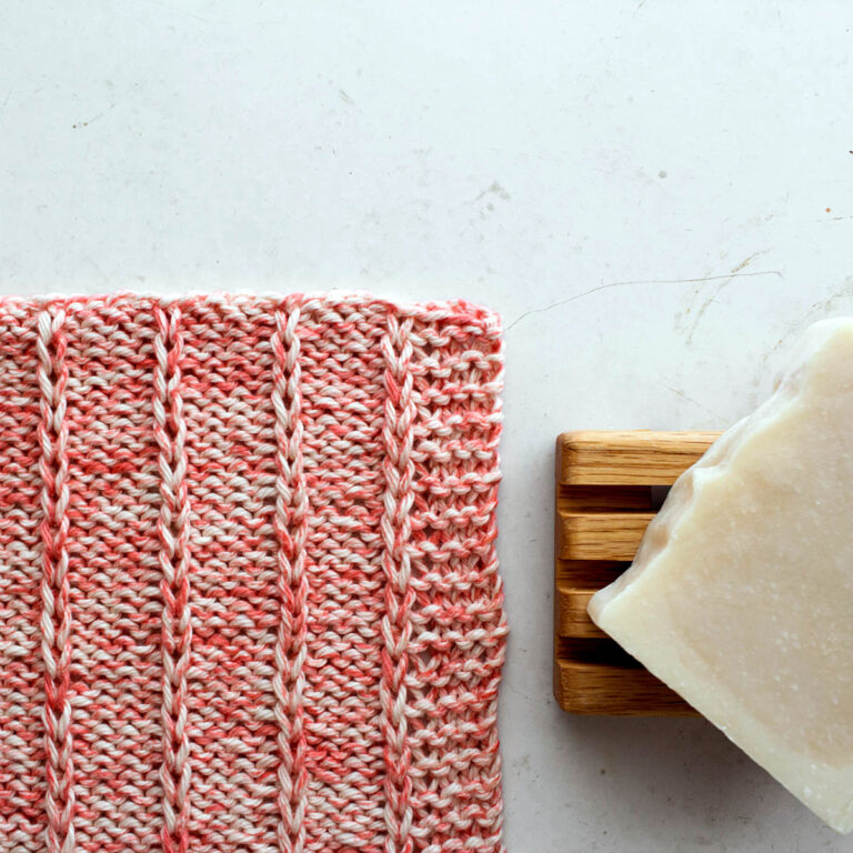 pic of a knit dishcloth on a table with a bar of soap on a wooden tray