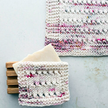 pic of a knitted eyelet dishcloth on a table with a bar of soap on a wooden tray
