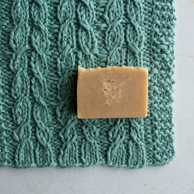 pic of a cable knitted dishcloth on a table with a bar of soap