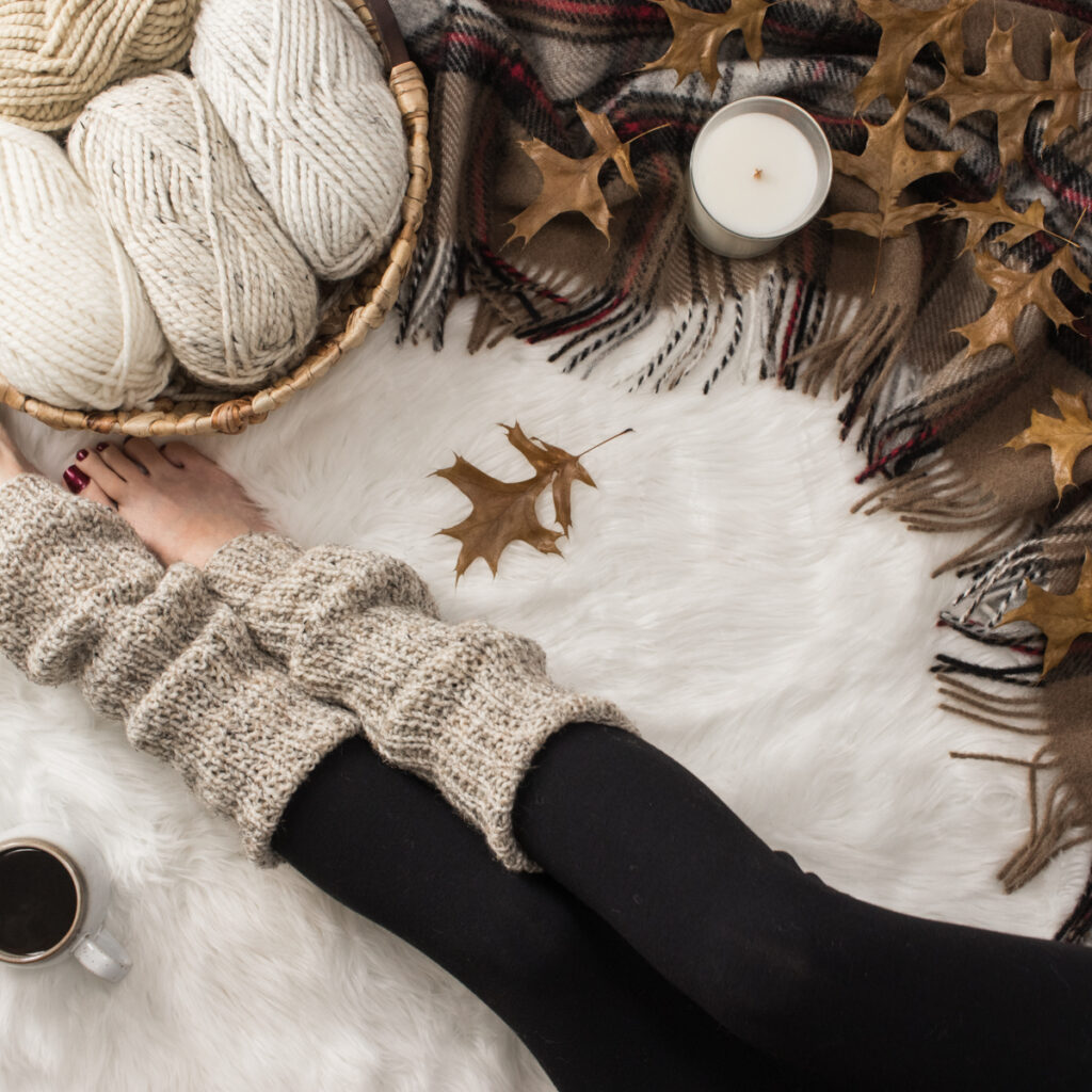 knitted leg warmers on a model in a cozy setting with a blanket coffee & balls of yarn