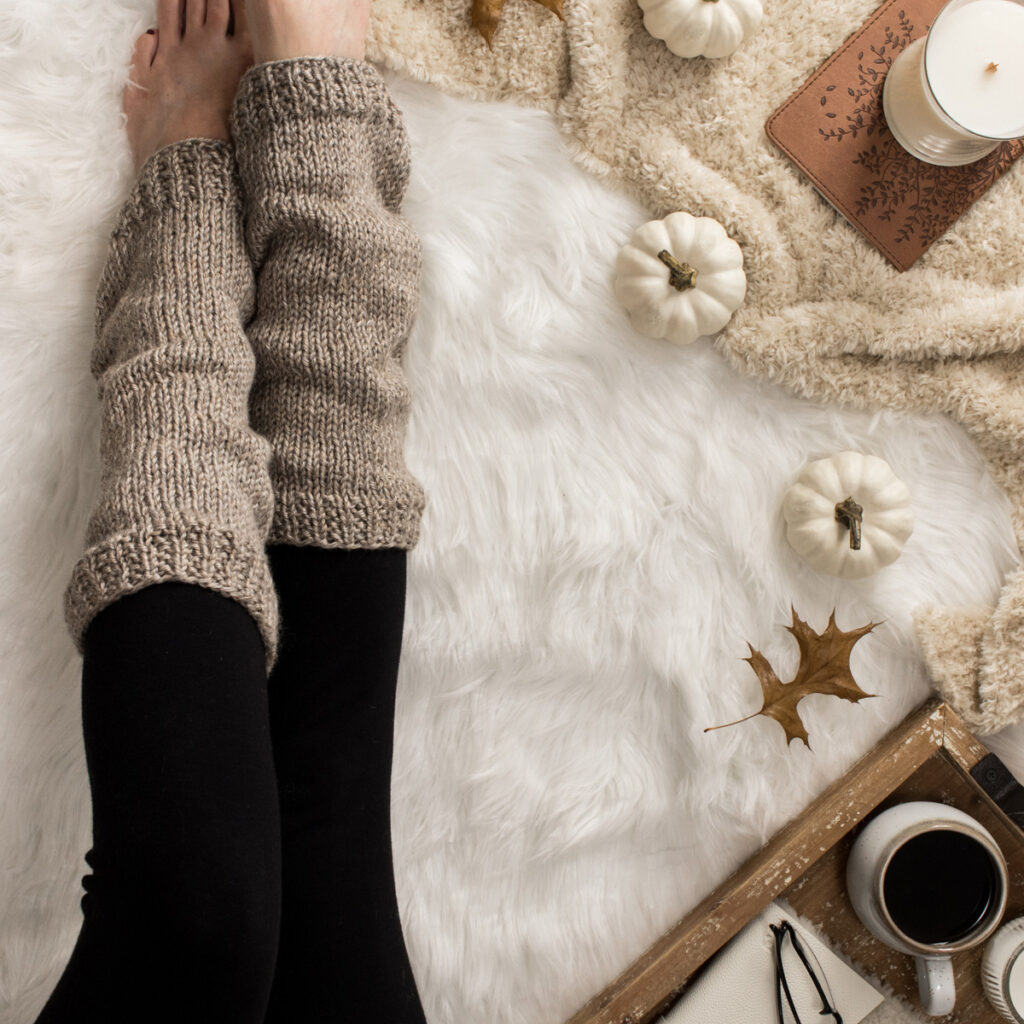 worsted weight knit leg warmers on a faux fur blanket in a cozy setting with candles, coffee & a journal