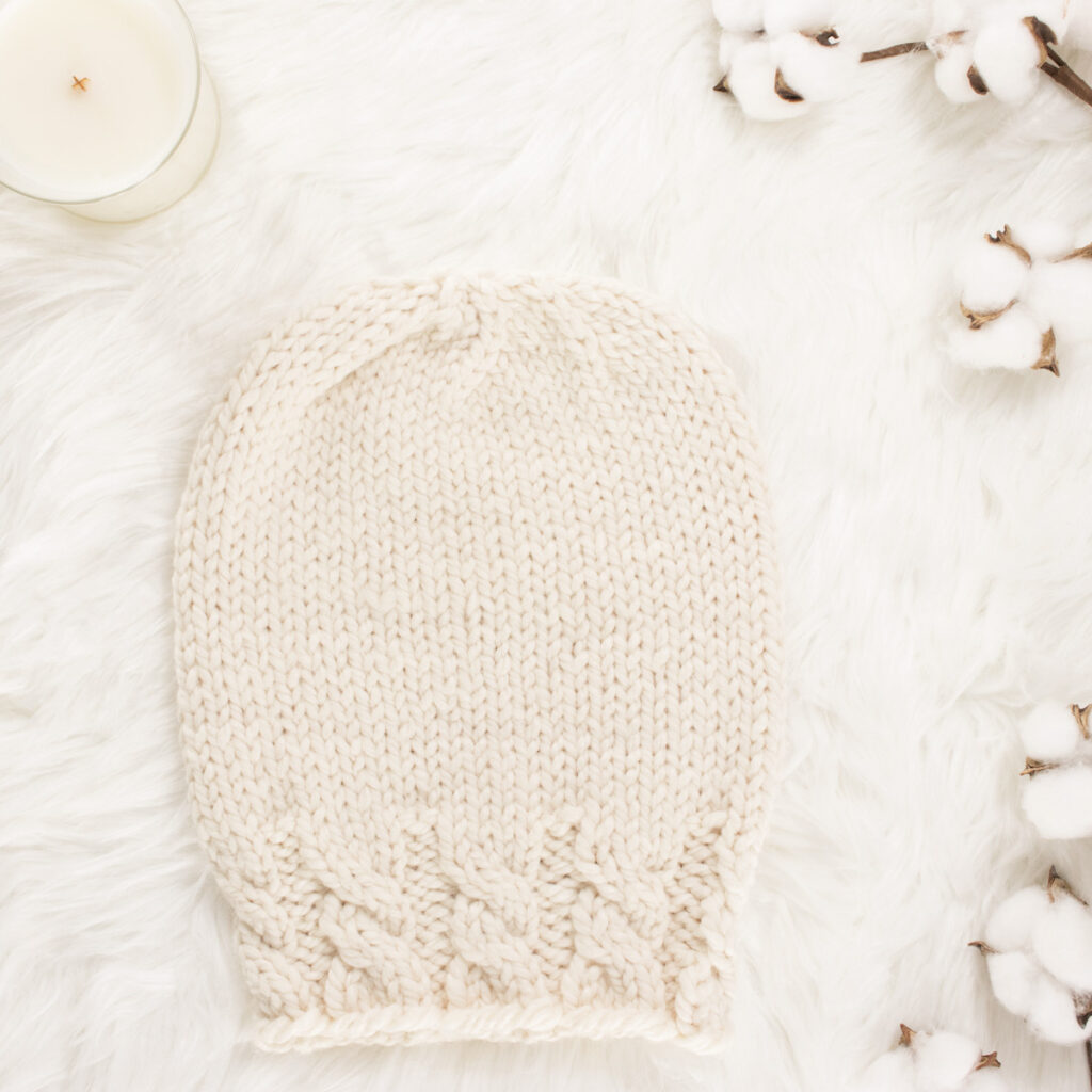 cozy scene of a hand knit chunky cable hat with cotton bolls & a candle