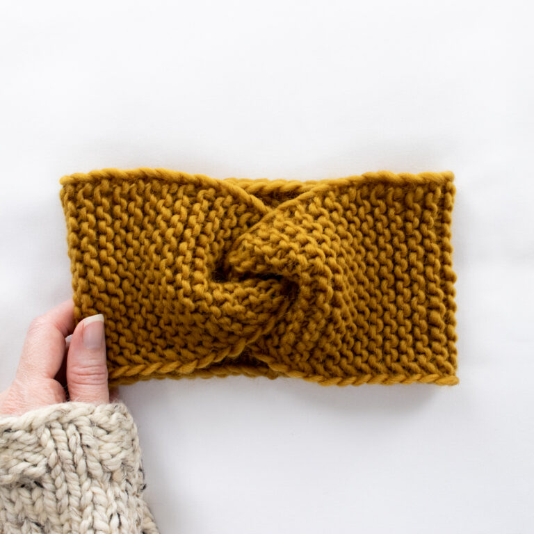 knitted headband laying flat with a hand wearing a sweater holding it.