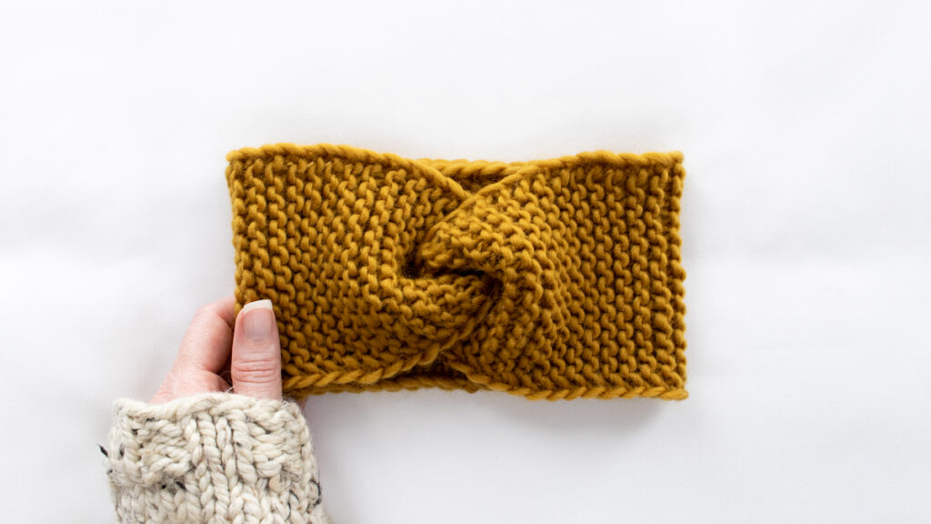 knitted headband laying flat with a hand wearing a sweater holding it.