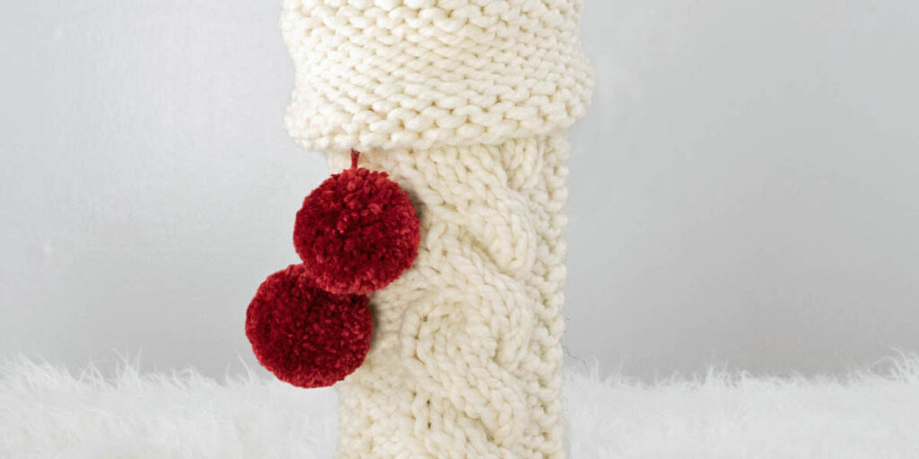 Christmas cable knitted wine bottle cover displayed on a wine bottle.