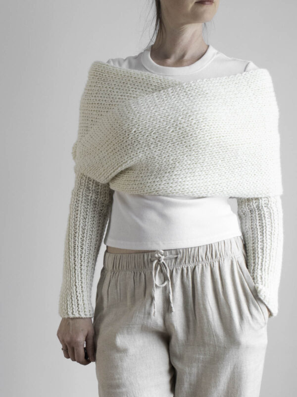 Side view of cream knit sweater scarf worn over white top with matching ribbed sleeves