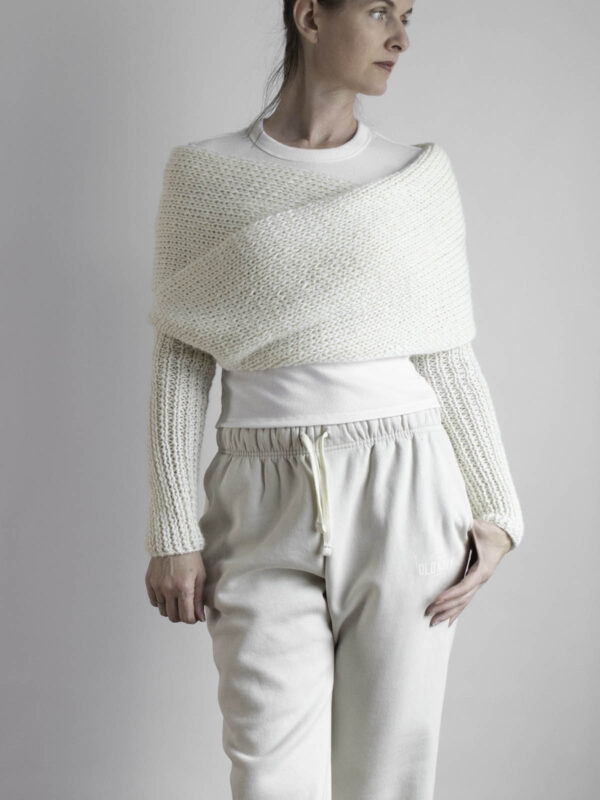 Cream sweater scarf with long knit sleeves styled over a cropped white top and beige joggers